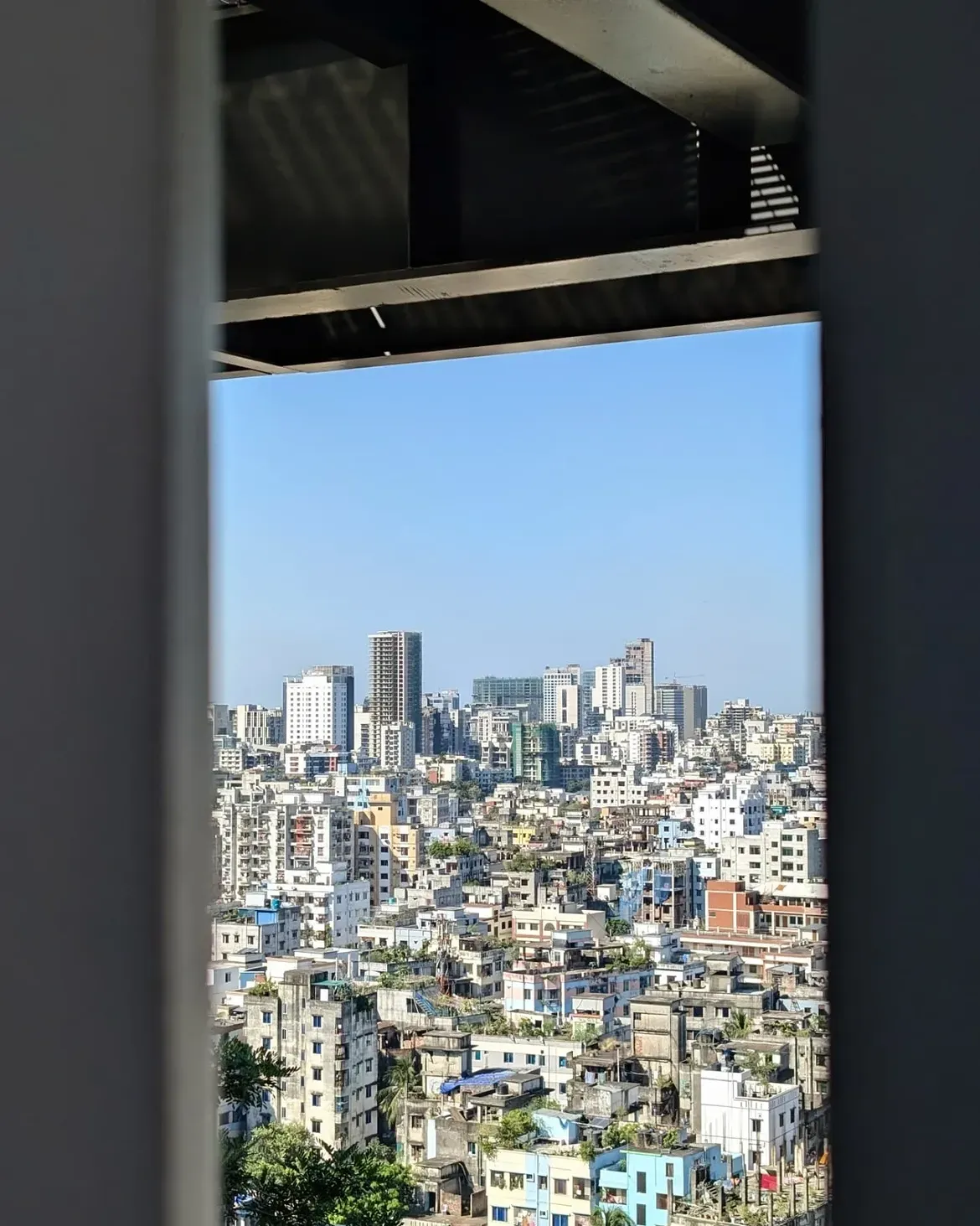 Dhaka skyline framed by dark columns and a roof overhang at BRAC University
